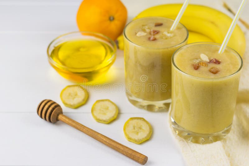 Frullati appena fatti con il mango, la banana, l'arancia, il miele, i dadi ed il cereale su una tavola di legno bianca immagini stock libere da diritti
