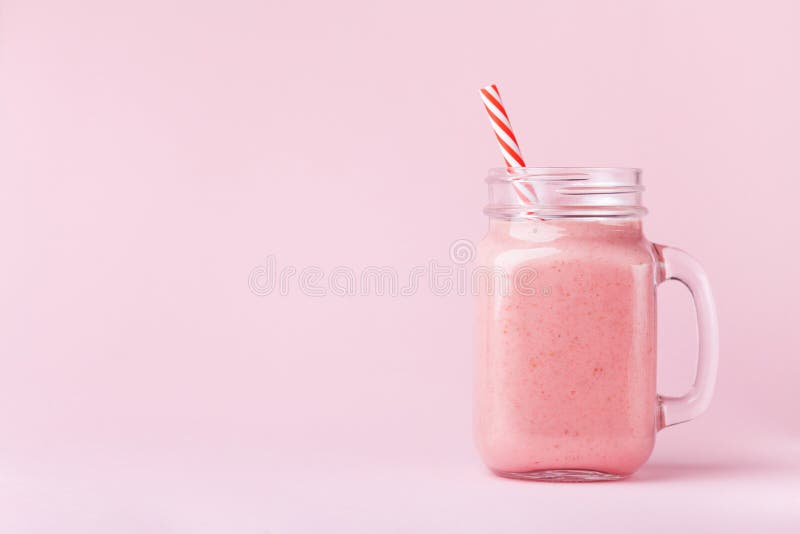 Frullato o frappé della fragola in barattolo di muratore su fondo pastello rosa Alimento sano per la prima colazione e lo spuntin