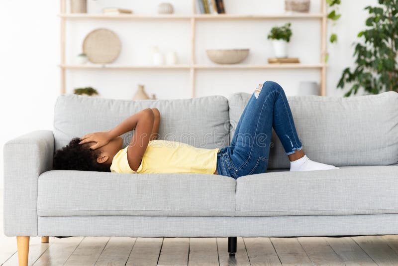 Frustrada chica negra llorando cara cubierta en el sofá en el interior imagenes de archivo