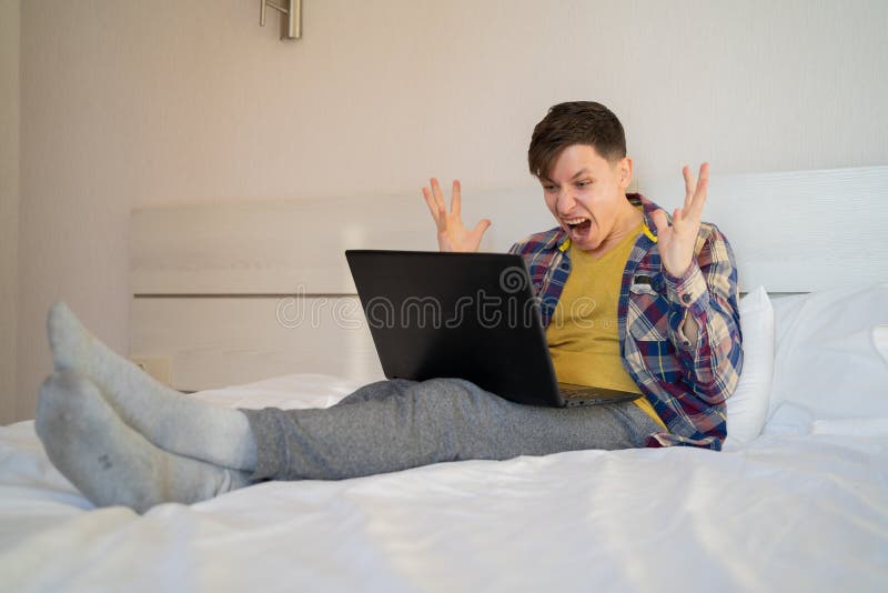 Frustrado hombre molesto sentado en la cama en la oficina de la casa usando una computadora mirando una laptop rota siente rabia y imagenes de archivo