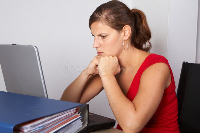 Young woman sitting at her laptop with a lot of work in front of her. She is very frustrated.