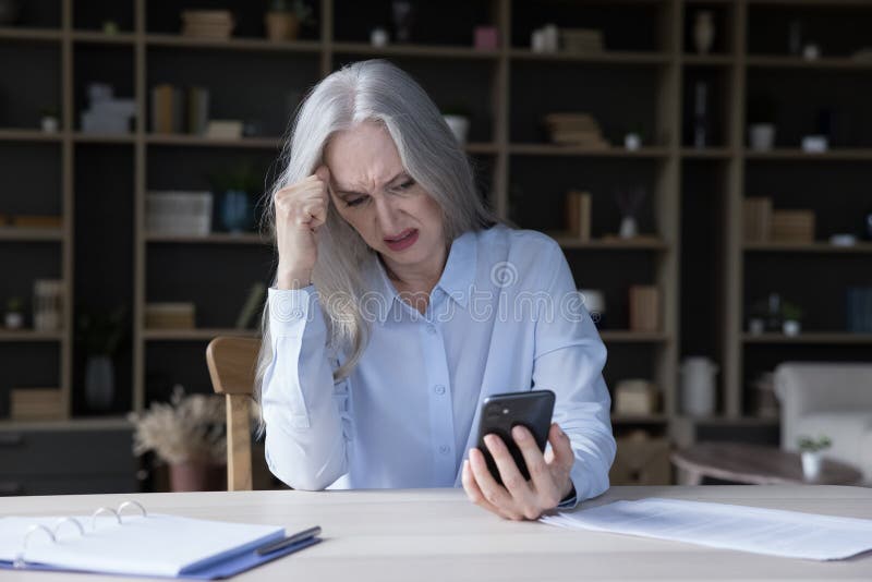 Frustrated annoyed elderly retired woman holding wrong working mobile phone