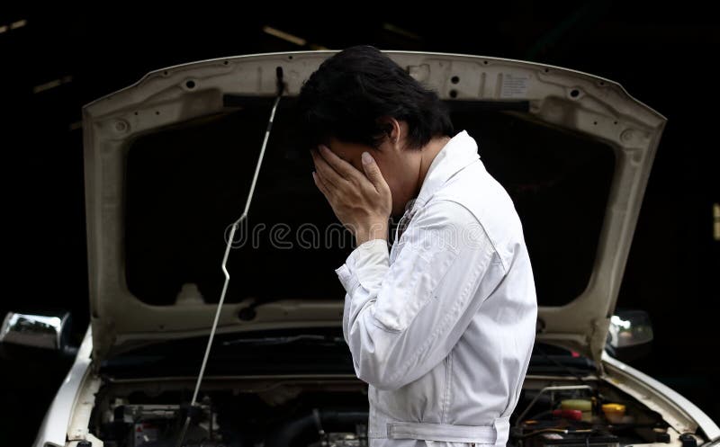 Frustrated ha sollecitato il giovane uomo del meccanico nel fronte della copertura dell'uniforme di bianco con le mani con l'auto fotografia stock libera da diritti Frustrated ha sollecitato il giovane uomo del meccanico nel fronte della copertura dell'uniforme di bianco con le mani con l'auto fotografia stock libera da diritti