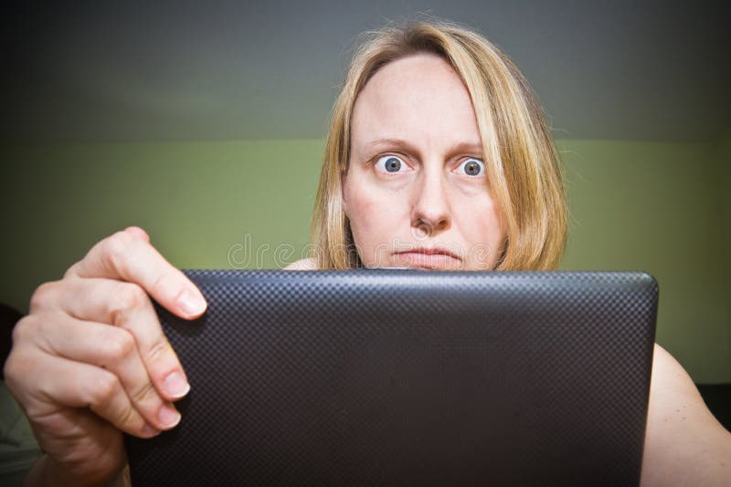 A woman with an angry and frustrated look on her face holding a laptop screen. A woman with an angry and frustrated look on her face holding a laptop screen.