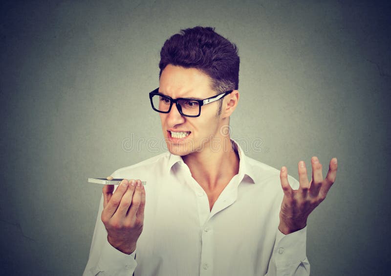 Frustrated man using a smart phone voice recognition function online. Frustrated man using a smart phone voice recognition function on line isolated on gray wall background