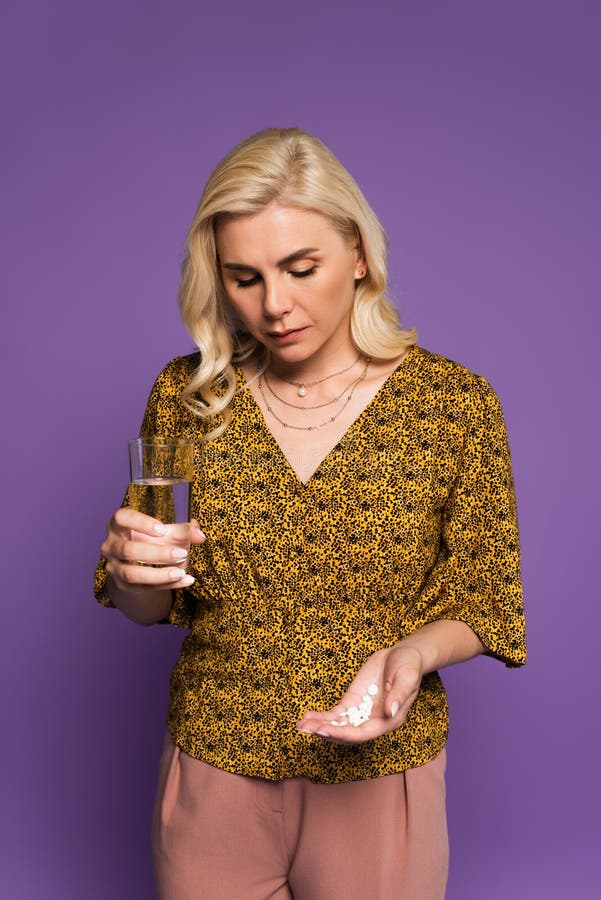 frustrated woman with climax holding pills and glass of water isolated on purple,stock image