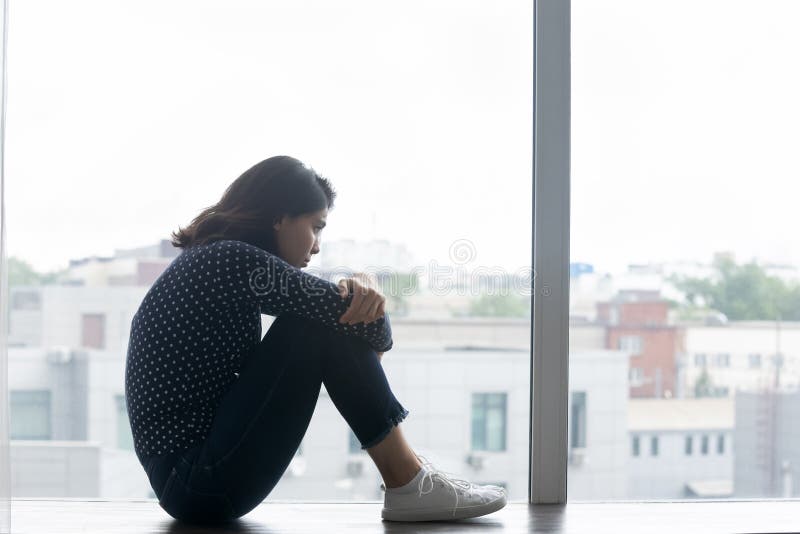 Frustrierte Einsamen asiatische Frau der Datenzugriffsseiten-Ansicht, die auf Fensterbrett sitzt lizenzfreie stockfotografie