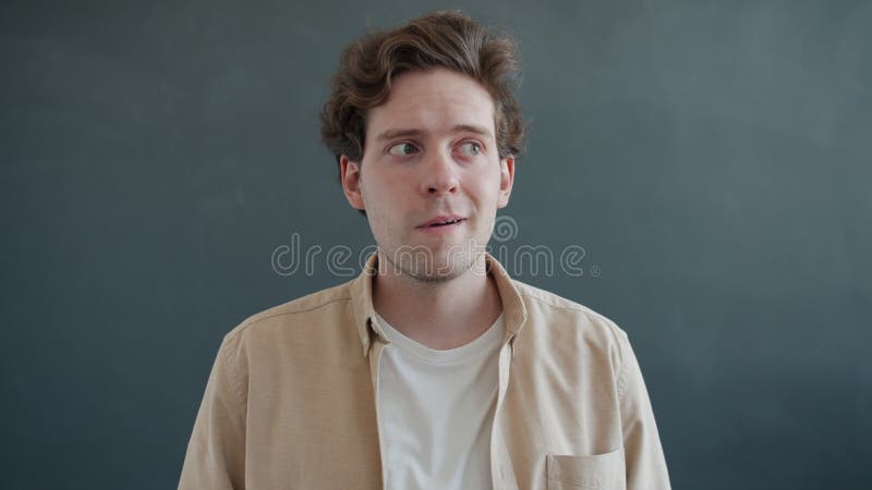 Frustré gars rotation des yeux regardant autour puis fixant la caméra avec le visage confus sur fond gris banque de vidéos