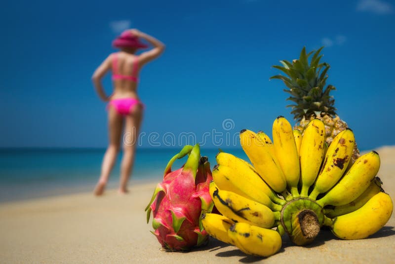 Frutas tropicales y una mujer en un bikini que toma el sol en la playa en fondo del mar. fotografía de archivo libre de regalías Frutas tropicales y una mujer en un bikini que toma el sol en la playa en fondo del mar. fotografía de archivo libre de regalías