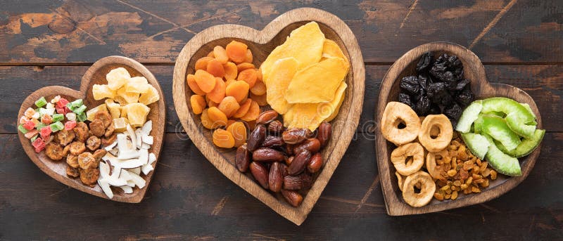 Healthy sweet dried fruits and berries in wooden heart shaped plates on wooden background. Healthy sweet dried fruits and berries in wooden heart shaped plates on wooden background