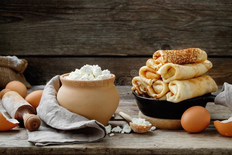 Frying pan of baked pancakes, ingredients and kitchenware for pancakes making on table.