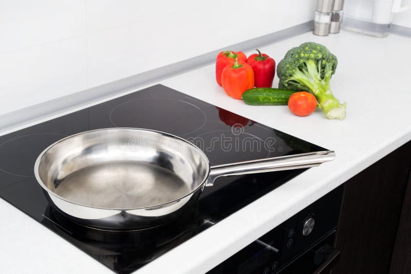 Frying pan and vegetables in modern kitchen. With induction stove stock photography