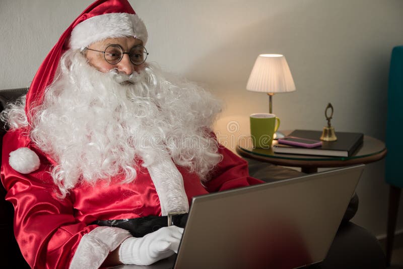 Från sidan av Santa Claus som kopplar av i den hemmastadda användande bärbara datorn fo för soffa arkivbilder Från sidan av Santa Claus som kopplar av i den hemmastadda användande bärbara datorn fo för soffa arkivbilder