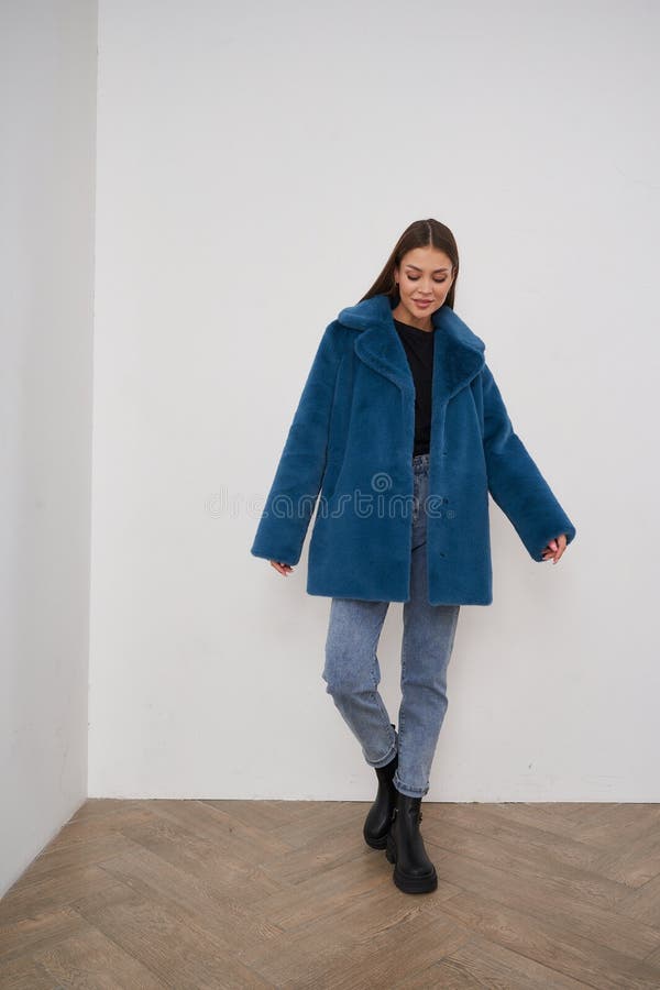 Fröhliche Brunette-Frau in blauer Jacke posiert drinnen mit Zuversicht und Stil stockbilder