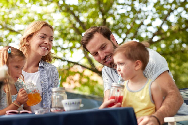 Fröhliche Familie sitzen im Freien trinken Säfte genießen. Vater hilft seinem Sohn, Saft auf Stroh zu trinken