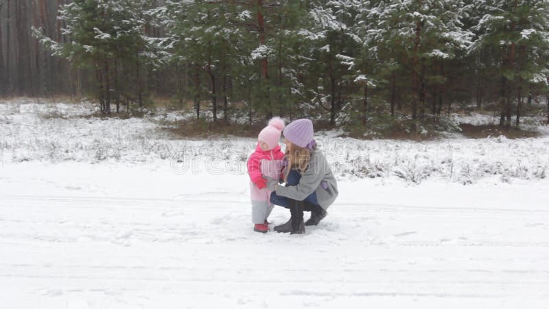 Fröhliche junge Mutter spielt mit ihrem kleinen Schneekind im Winterwald