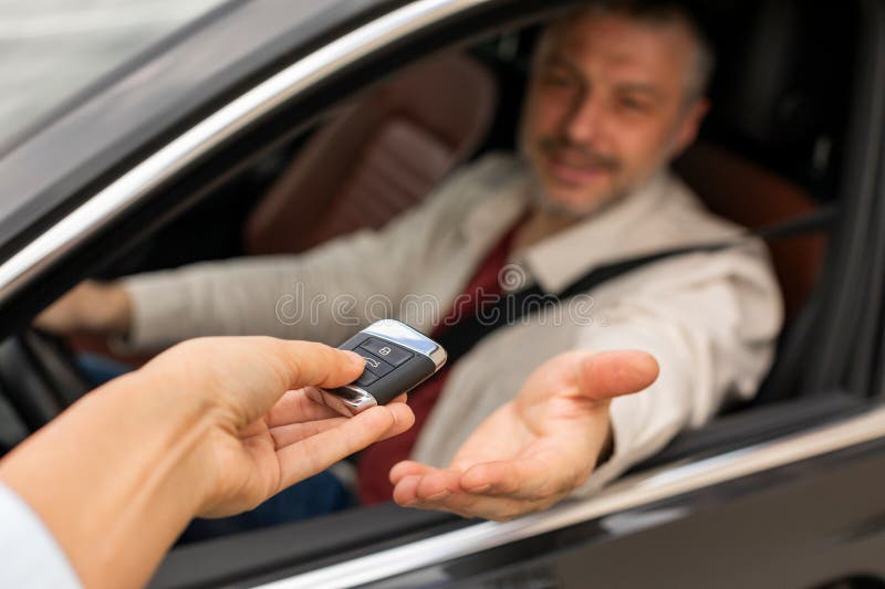Fröhlicher Mann mittleren Alters, der in einem neuen Auto sitzt und den automatischen Autoschlüssel vom Leasing- oder Mieterin übe stockbilder