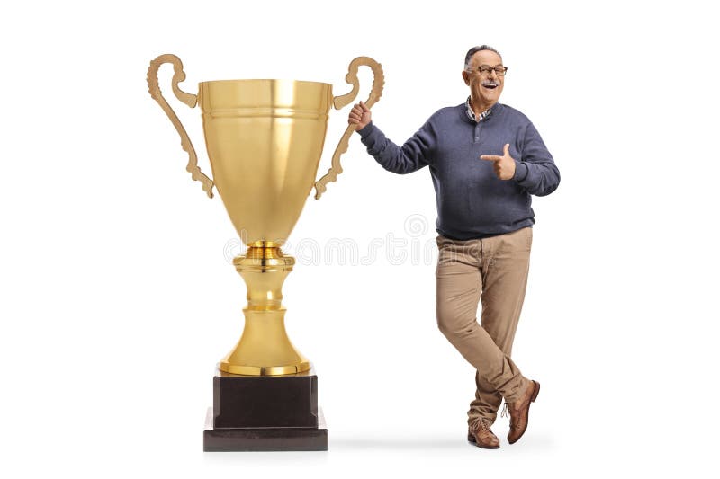 Fröhlicher reifer Mann, der auf eine große Goldtrophetasse zeigt lizenzfreies stockbild