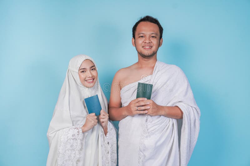 Fröhliches asiatisches Muslimpaar in ihram und Gebetskleid, das mit einem Pass, abgeschirmt durch blauen Hintergrund posiert. Hads lizenzfreies stockbild