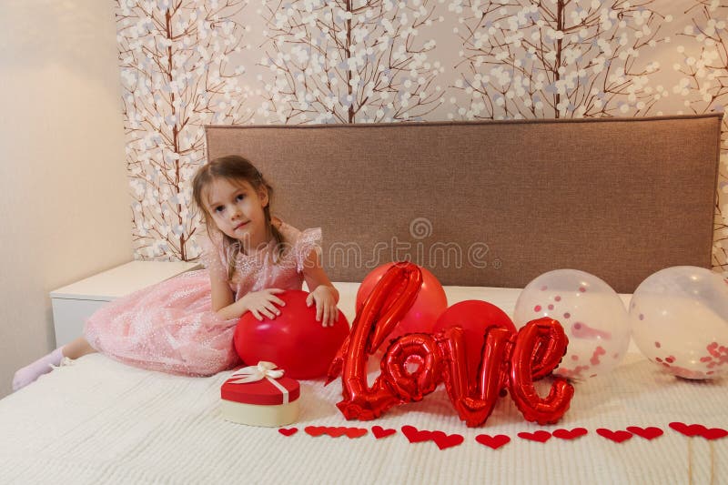 Fröhliches kleines Mädchen sitzt auf der Decke mit herzerförmigen Ballons lizenzfreies stockbild