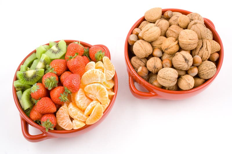 Two red bowls, one with three colour fruits red strawberries, orange mandarines and gren kiwis, and the other one with mixed nuts walnuts, hazelnuts, almonds. White background, isolated. Two red bowls, one with three colour fruits red strawberries, orange mandarines and gren kiwis, and the other one with mixed nuts walnuts, hazelnuts, almonds. White background, isolated.