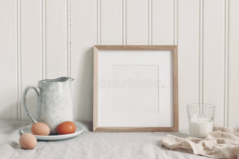 Frühlingsfrühstücks-Stilllebenszene Leeres Holzrahmenmodell des Quadrats mit Hühnereier, Glas Milch und keramischem Krug