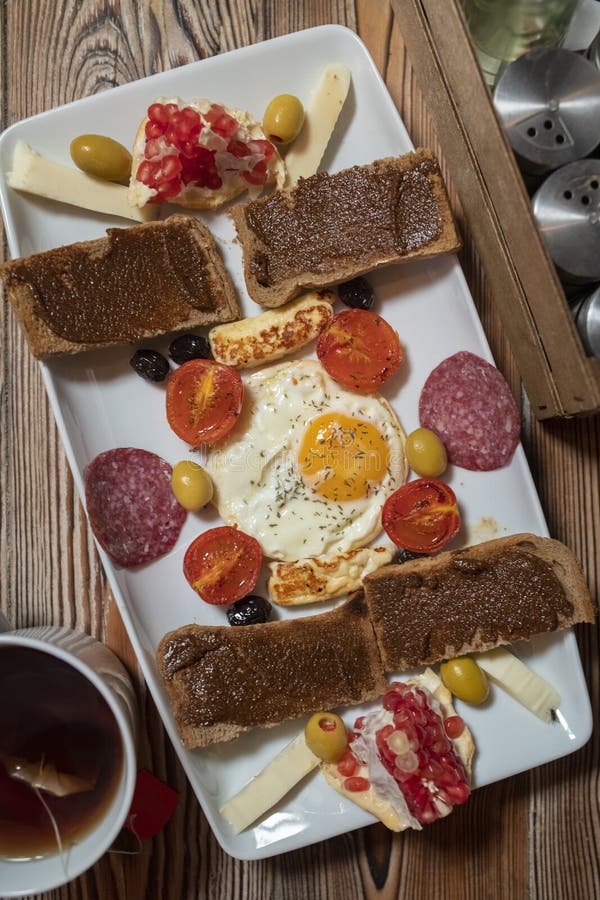 Frühstück mit Spiegelei, Roggenbrot, Granatapfel, Johannisbrotbaumpaste, Käsen, Oliven, trockener Salami, Tomaten und Tee lizenzfreie stockfotos Frühstück mit Spiegelei, Roggenbrot, Granatapfel, Johannisbrotbaumpaste, Käsen, Oliven, trockener Salami, Tomaten und Tee lizenzfreie stockfotos