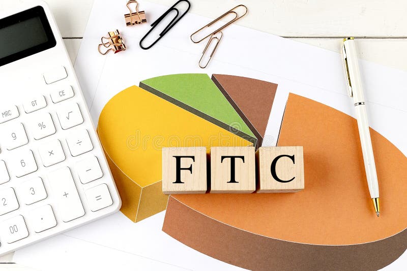 FTC text on wooden blocks placed on a pie chart with a calculator, stationery, and pen on a white desk stock image