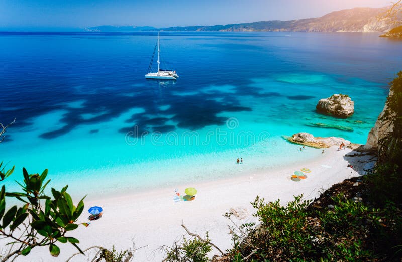 Fteri strand, Cephalonia Kefalonia, Grekland Vit katamaranyacht i klart blått havsvatten Turister på den sandiga stranden nära royaltyfria foton Fteri strand, Cephalonia Kefalonia, Grekland Vit katamaranyacht i klart blått havsvatten Turister på den sandiga stranden nära royaltyfria foton