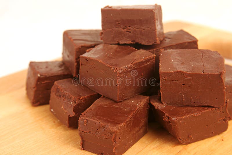 A closeup shot of a stack of homemade chocolate fudge on a wood cutting board. A closeup shot of a stack of homemade chocolate fudge on a wood cutting board.