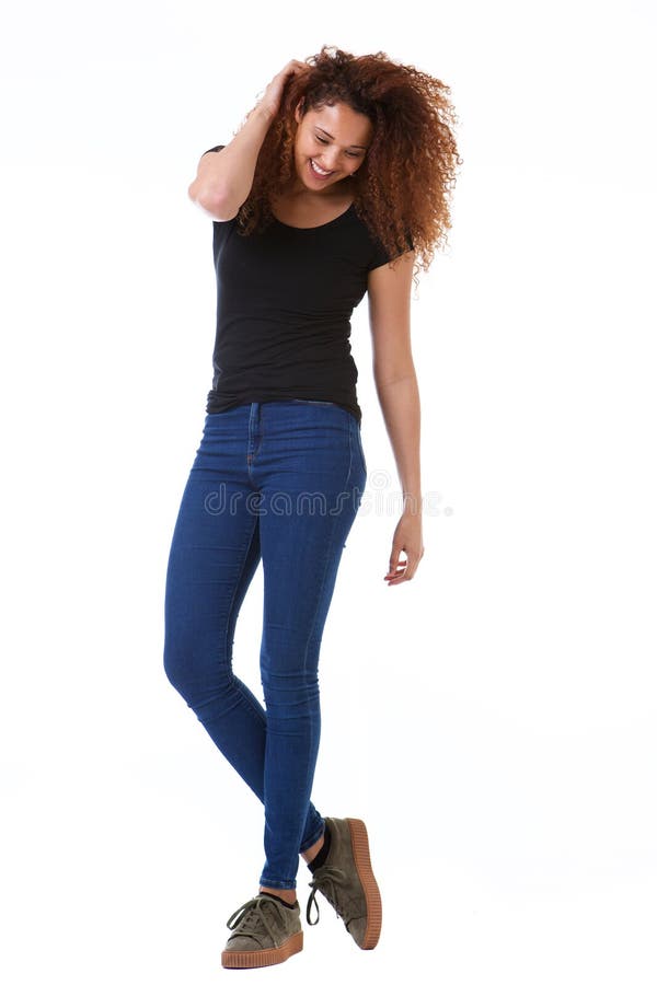 Full body happy young woman with hand in curly hair standing against isolated white background