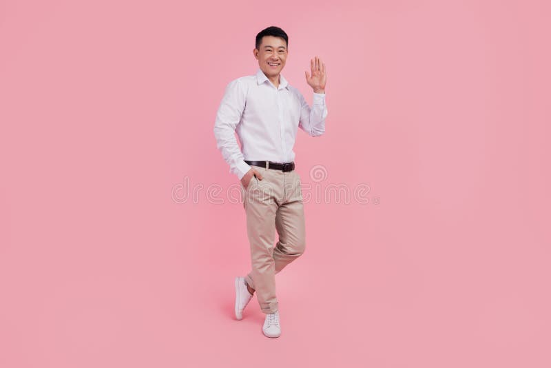 Full body photo of young asian man waving hand hello greeting friendly isolated over pink color background stock image