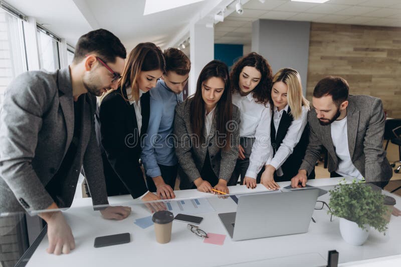 Full concentration at work. Group of young business people working and communicating while standing in modern office royalty free stock photo Full concentration at work. Group of young business people working and communicating while standing in modern office royalty free stock photo