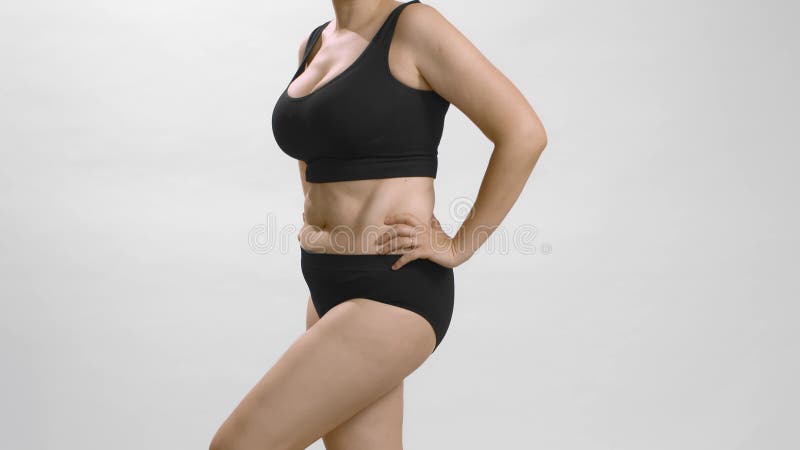 Full figure body positive caucasian woman in black underwear turns around and appreciate her body. White studio