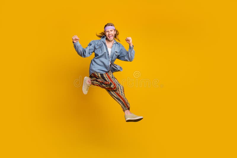 Full size photo of cool young man raise fists jump empty space wear denim shirt isolated on yellow color background. Full size photo of cool young man raise fists jump empty space wear denim shirt isolated on yellow color background.