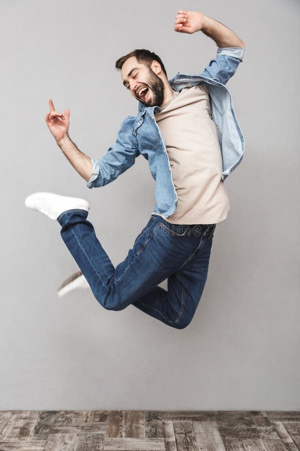 Full length portrait of a happy young man wearing shirt jumping over gray background, celebrating