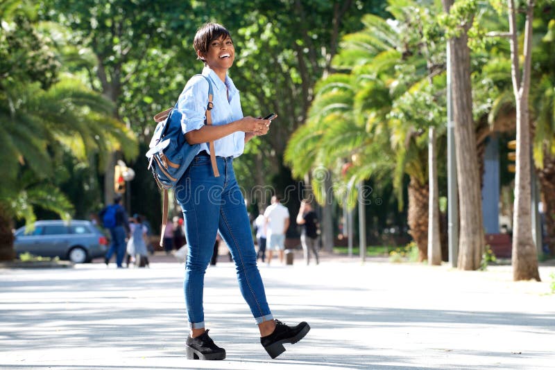 Full length attractive young african woman walking with bag and mobile phone