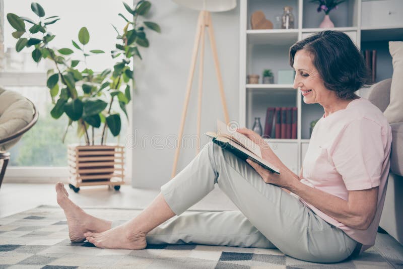 Full length body size side profile photo senior woman sitting on floor in casual clothes reading book spending free time