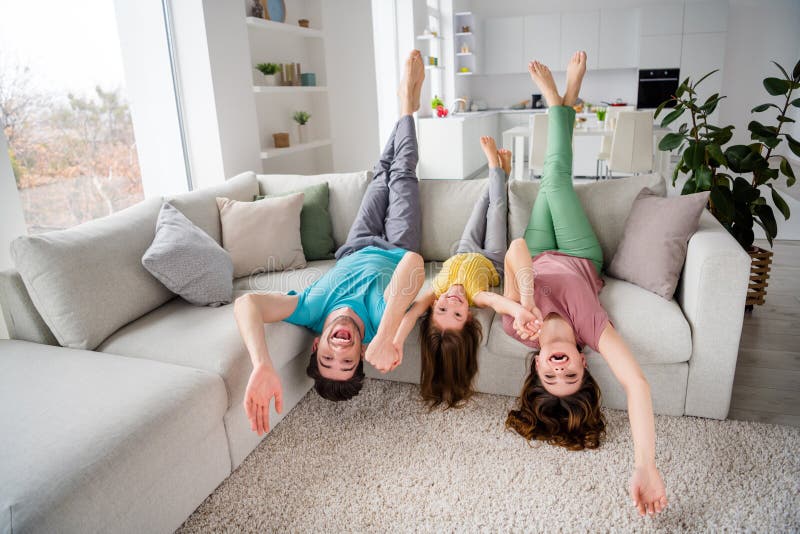 Full length photo of three people have family relax weekend sit couch upside down hold hand in house indoors