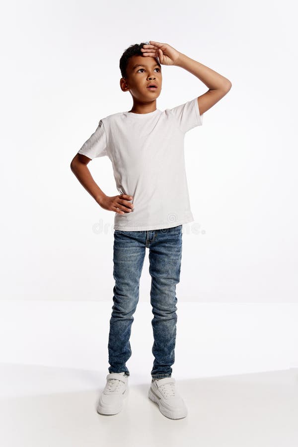 Full-length portrait of african little boy in white tee looking up isolated over white background. Kids emotions concept