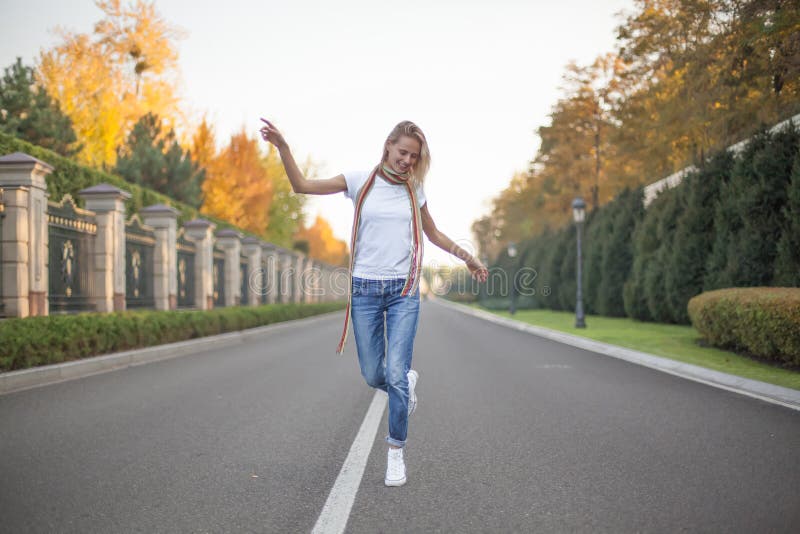 A full-length portrait of a beautiful blonde who dances in the middle of a road in a large park. Hands raised to the side stock image A full-length portrait of a beautiful blonde who dances in the middle of a road in a large park. Hands raised to the side stock image