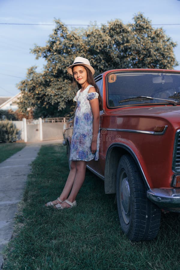 Full length portrait, beautiful young brunette little girl in dress and hat leaned on the red old antique car and stock photography Full length portrait, beautiful young brunette little girl in dress and hat leaned on the red old antique car and stock photography