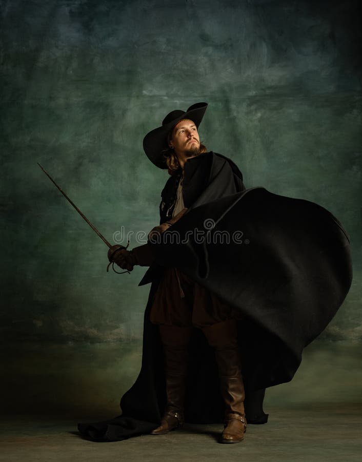 Full-length portrait of fearless brutal man, medeival pirate in hat and cloak with sword isolated over dark background.