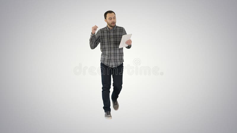 Man in casual walking with tablet and talking via videoconference on gradient background.