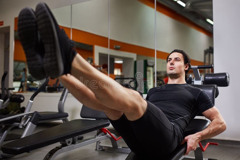 Full length portrait of muscular build man while doing legs press exercise in fitness center.