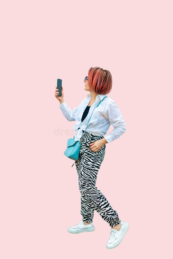 Full length portrait of a pink-haired girl in a white shirt holding smartphone on a pink background