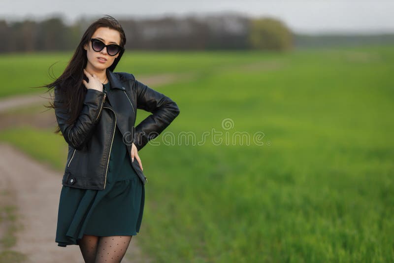 Full length portrait of a stylish girl walking along a green field. A young smiling woman is walking in nature. Green