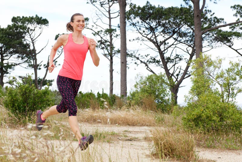 Full length portrait of woman smiling while running trail outside stock photography Full length portrait of woman smiling while running trail outside stock photography