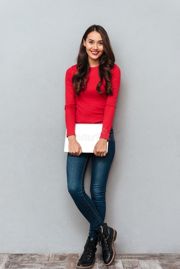 Full length portrait of young beautiful woman in casual wear holding laptop, looking at camera royalty free stock photography Full length portrait of young beautiful woman in casual wear holding laptop, looking at camera royalty free stock photography