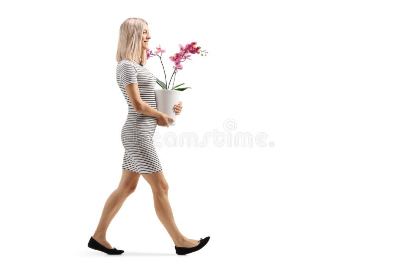 Full length profile shot of a young woman walking a carrying an orchid flower pot